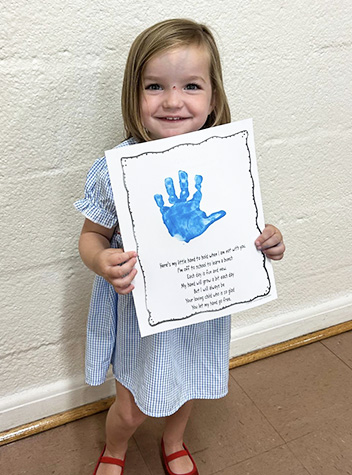 Preschool girl holding up a handprint and smiling for the camera