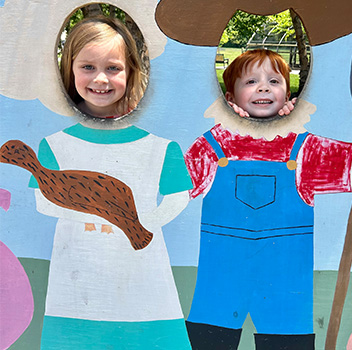 sidebar_ChooseUsi_061520 two students with their faces in a display that looks like they are farmers