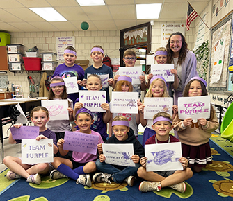 Classmates dressed in purple and holding up posters
