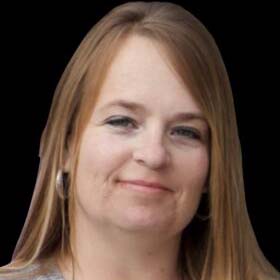 A headshot of Michelle Williams, a Caucasian woman with long light brown hair and a warm smile. She is wearing a gray sweater and large silver hoop earrings against a black background.