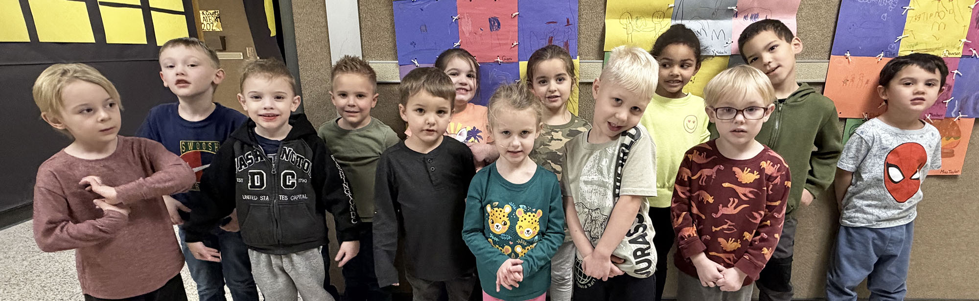 Group of elementary students posing for a picture in front of a bulletin board
