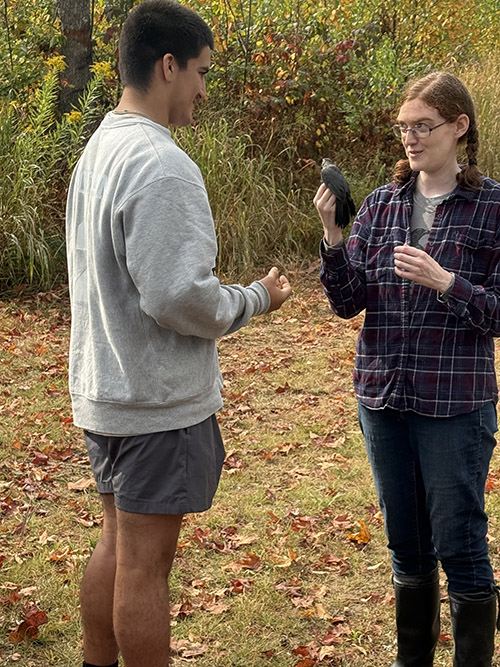 Student talking to a woman holding a bird in the forest