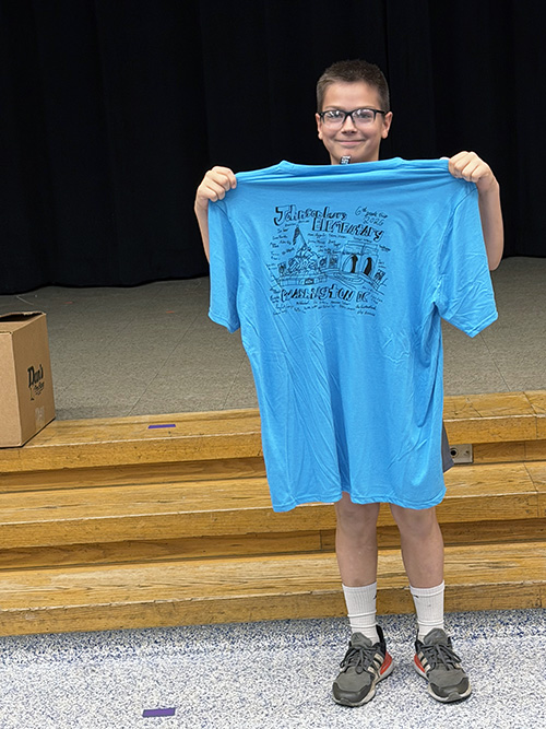 6th grade student holding up his blue Washington T-shirt