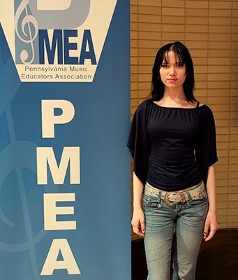 Female student next to PMEA, Pennsylvania Music Education Association banner selected for All State