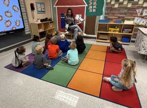 students on the floor listening to an adult read a book