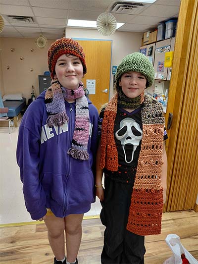Two students wearing handmade scarves and hats