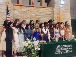 Group of students dressed in nice attire behind a table with a Cloudcroft banner