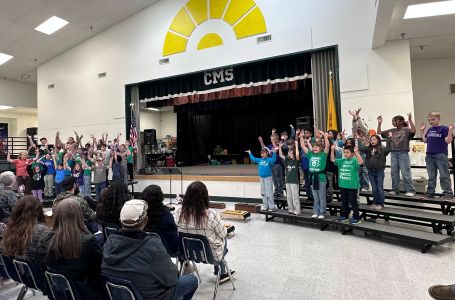 group of elementary students performing on risers in a multi-purpose room for seated parents