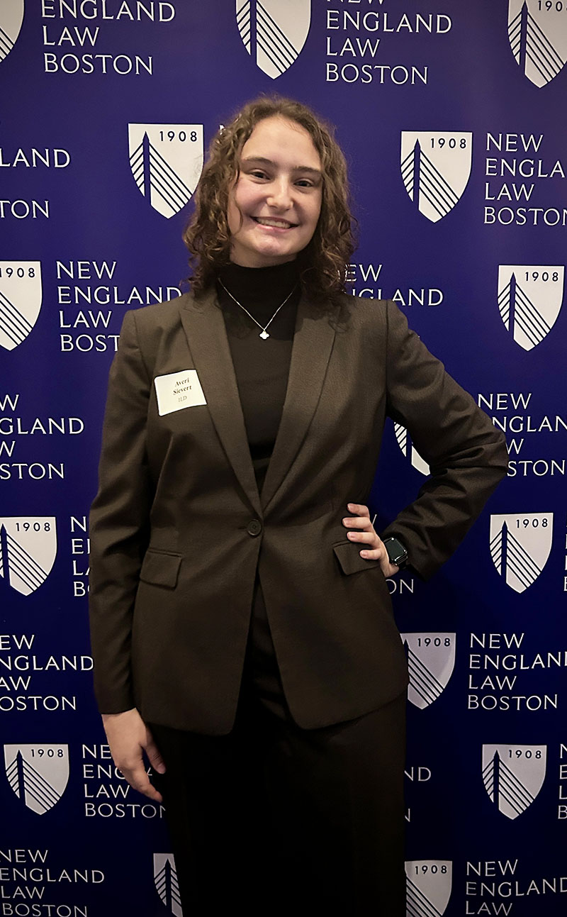 Averi Sievert posing for a picture in front of a New England Law Boston panel