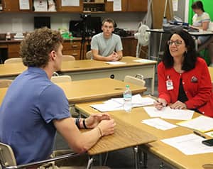 Teacher in red blazer talking with student across from a desk