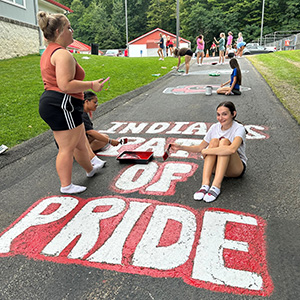 Adults and students outside painting Indians Pride mural on a road