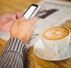 Parent checking his phone next to a cup of coffee