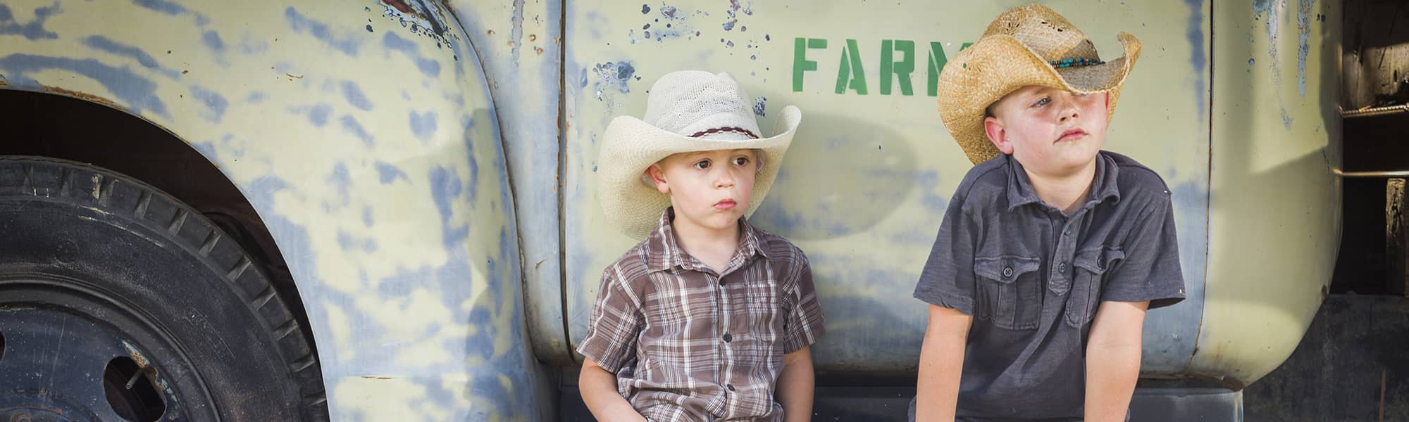 Two young cowboys sitting next to a farming truck
