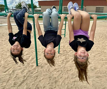 Three students hanging upside down on the playground bars