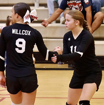 Two students shaking hands while playing volleyball