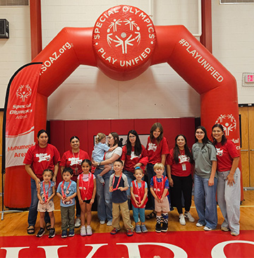Students and staff standing under a Special Olympics -Play Unified inflatable goal post