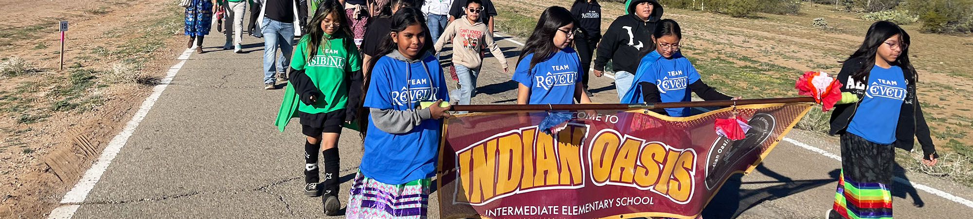 Happy students outside marching with an Indian Oasis Intermediate Elementary School banner