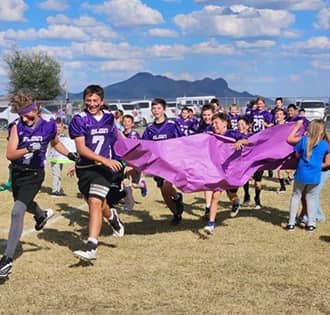 football team running with a purple banner