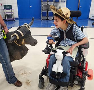Smiling boy in a wheelchair looking at a bull-shaped bag