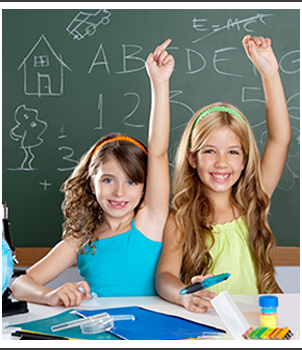 Two girls in a classroom with their hands raised